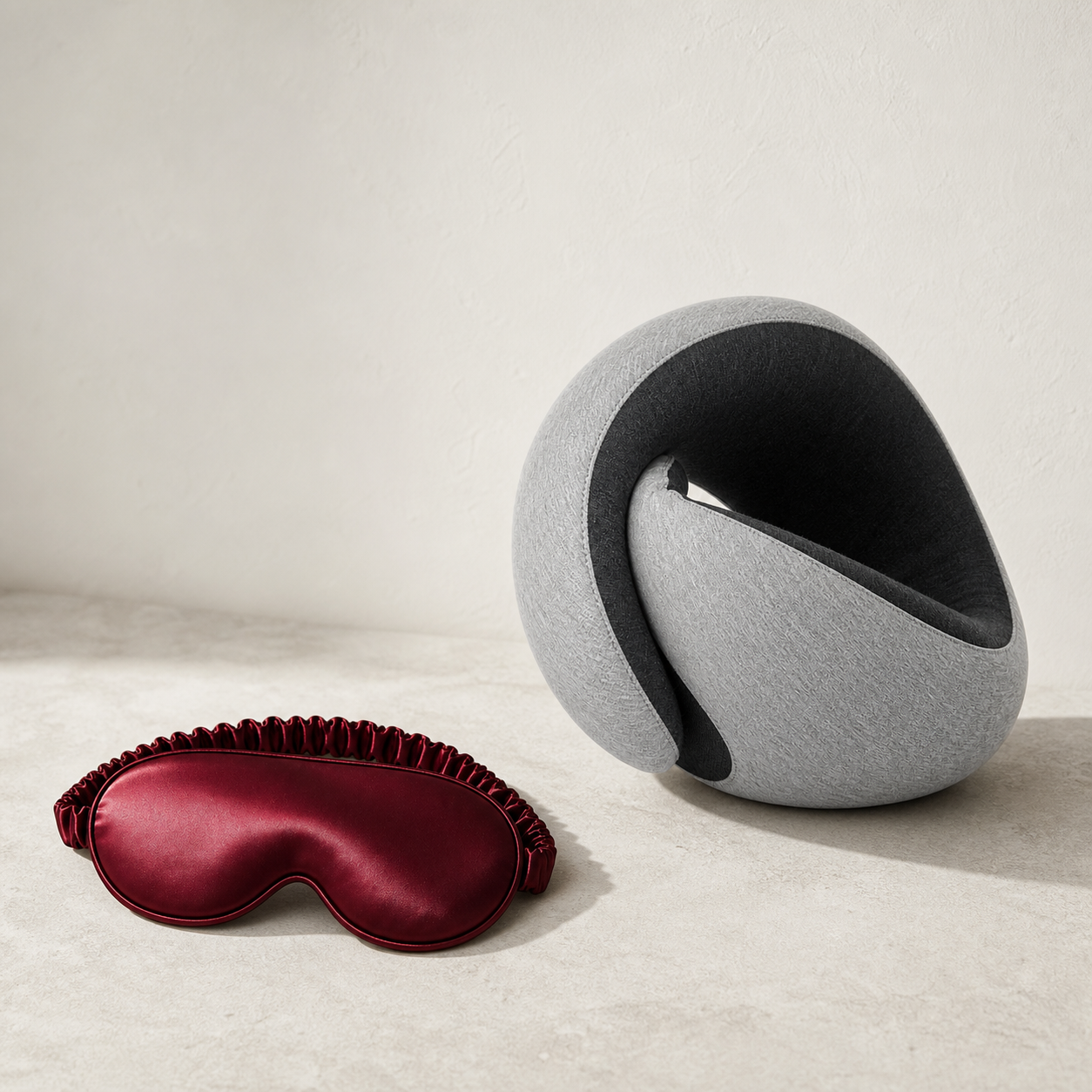 Dormio Sleep Travel Set: Bordeaux Seidenmaske neben dem hellgrauen Cocoon Reisekissen